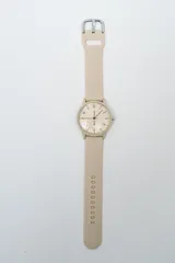 Reloj analógico con caja redonda color beige y correa de silicona beige. La esfera es minimalista con números arábigos y manecillas negras. Posee un broche metálico plateado.