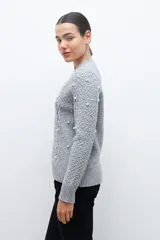 Sweater color beige melange de tejido de punto con diseño de trenzas y detalles de perlas en el frente y las mangas.