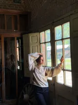 Buzo de punto color crema con diseño oversize, cuello redondo y mangas largas abullonadas. Presenta detalles de costuras decorativas en contraste y apliques de flecos colgantes en la parte frontal y mangas.