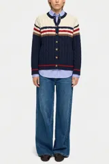 Saco tejido de punto con diseño de bloques de color en azul marino, crema, rojo y marrón. Presenta cierre frontal con botones, cuello redondo y textura de cableado en el tejido.