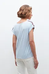 Blusa celeste con estampado floral en tonos marrones, de corte clásico, cuello en V y mangas cortas.