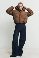Campera puffer acolchada de color negro, con cuello envolvente, capucha integrada, manga larga, bolsillos laterales ocultos y bajo con elástico. Cierre frontal con botones a presión ocultos por solapa.