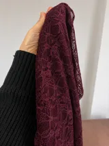 Vestido corto de encaje negro con mangas largas y cuello redondo. Presenta un diseño ajustado con un detalle de fruncido lateral en la falda que crea un efecto de caída asimétrica.