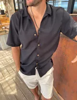 Camisa de fibrana negra de manga corta, con cuello solapa y cierre frontal de botones claros.