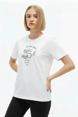 Remera de manga corta de algodón, color blanco, con cuello redondo y estampado frontal estilo collage con gráficos y texto en tono bordó.