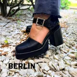 Zapatos de cuero negro con plataforma, taco ancho y tira en el tobillo con hebilla metálica.