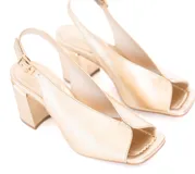Zapato de cuero color dorado, con taco cuadrado y punta abierta. Presenta una tira fina con hebilla al tobillo.