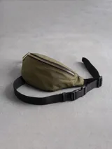 Riñonera de nylon color verde militar con cierre metálico dorado y correa ajustable de cinta negra con hebilla de plástico.