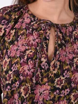 Blusa estampada con flores en tonos rosa, negro y verde. Tiene cuello redondo con abertura en forma de lágrima y mangas largas con puños elásticos.