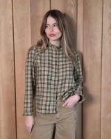 Camisa de algodón a cuadros en tonos verde, blanco y marrón, con cuello alto con volados, cierre frontal de botones y mangas largas con puños con volados.