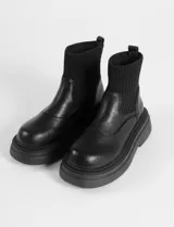 Botas tipo chunky de cuero sintético negro, con caña elastizada de tejido acanalado y suela gruesa dentada.