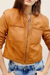 Saco corto de cuero ovino en color tostado, sin cuello, con detalles de trenzados en los bordes y bolsillos frontales con solapa.