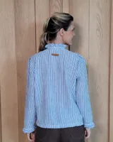 Camisa de manga larga con estampado de rayas verticales en tonos crudo y beige. Presenta cuello alto con volados, cierre frontal con botones dobles y puños con volados.