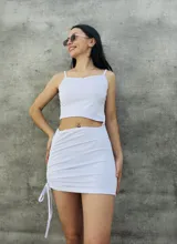 Conjunto blanco de top corto con breteles finos y falda corta con frunce lateral y cordones ajustables.