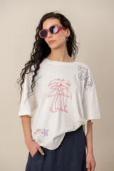 Remera blanca de manga corta y corte oversize, con bordados de motivos tropicales y marinos como palmeras, peces, estrella de mar y caracol.