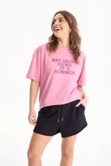 Remera de algodón rosada con estampa frontal en tono burdeos con la inscripción "BREAKING NEWS IT'S SUMMER", de manga corta y corte holgado.
