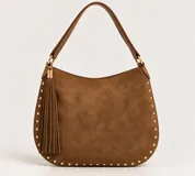 Cartera estilo hobo de color marrón con textura tipo gamuza, detalle de flecos colgantes y tachas doradas a lo largo de los bordes. Cuenta con asa para el hombro y herrajes metálicos dorados.