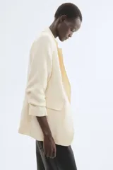 Blazer entallado color beige en mezcla de viscosa, con hombreras, solapas de muesca, bolsillos delanteros con solapa y mangas tres cuartos fruncidas. Diseño sin cierre y con forro interior.