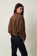 Campera de gamuza marrón, de corte oversize con hombros caídos, cuello camisero, cierre frontal de cremallera y puños y dobladillo elásticos.