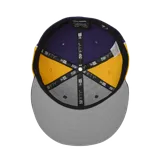 Gorra tipo cap de visera plana, colaboración entre Corteiz y New Era. Presenta un diseño bicolor en violeta y amarillo, con el logo de Corteiz bordado en blanco en el frente y el logo de New Era en el lateral.