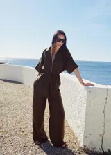 Pantalón palazzo marrón de tiro medio, con cintura elástica ajustable, bolsillos laterales y diseño largo de pernera ancha.
