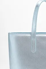 Bolso tipo tote en color celeste metalizado, con doble asa superior y costuras pespuntadas visibles.