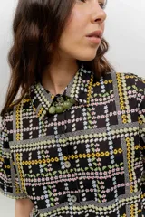 Vestido camisero corto con estampado a cuadros en tonos verde, azul y rojo. Presenta cuello camisero, mangas corta, cierre frontal con botones y falda tableada de corte bajo.