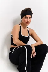 Conjunto deportivo compuesto por un top de escote redondo y calzas de tiro alto con diseño acampanado. Ambas piezas son de color negro con detalles de costuras blancas en contraste y logo estampado en el frente del top.