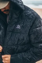 Campera puffer con capucha, color negro, con cierre frontal y diseño acolchado. Presenta un acabado con efecto mojado y logo pequeño en el pecho.