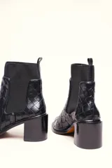 Bota tipo botineta de cuero negro con diseño trenzado artesanal en toda la capellada. Presenta paneles laterales elásticos, taco cuadrado de altura media y tirador en la parte superior trasera.