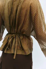 Camisa marrón a rayas con cuello redondo, mangas largas anchas y puños rectos. Cuenta con cierre frontal de botones y un lazo cinturón ajustable del mismo tejido en la cintura.