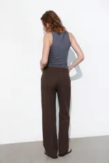 Pantalón de corte recto y tiro bajo, color marrón oscuro. Presenta trabillas en la cintura, bolsillos laterales, falsos bolsillos traseros de vivo y raya planchada en el delantero. Cierre frontal con cremallera, botón interior y ganchos metálicos.