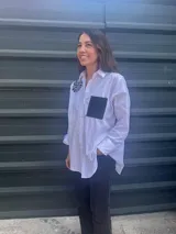 Camisa blanca de corte clásico con bordado de hilo negro en el hombro y bolsillo de cuerina negro en el pecho.