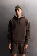 Sudadera de hombre Zara Athleticz de ajuste relajado (relaxed fit), color marrón, confeccionada en tejido técnico compacto con mezcla de algodón y elasticidad. Cuenta con cuello con capucha ajustable con cordones negros, manga larga, bolsillo frontal tipo canguro con un pequeño bolsillo termofijado con cierre, y acabados con rib en puños y cintura.