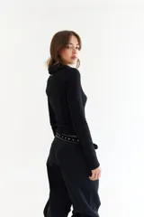 Top de manga larga color verde petróleo, con cuello polo y escote en V pronunciado. Presenta recortes diagonales en el frente y un pequeño bordado en el puño.