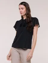 Blusa blanca elegante con cuello con lazo integrado para anudar al frente, escote en V sutil y mangas cortas estilo mariposa de gasa translúcida.