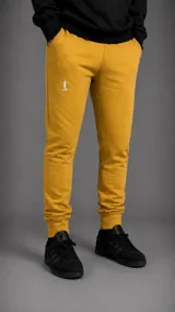 Pantalón tipo jogger color mostaza, con corte ajustado, cintura elástica con cordón y puños acanalados en los tobillos. Presenta un pequeño logo bordado en color blanco en la parte superior del muslo.