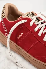 Zapatillas rojas de gamuza con cordones color beige y suela marrón. Detalle de animal print en el talón y pespuntes blancos.