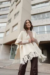 Ruana de lana tejida en color crudo, con diseño de textura en relieve y terminación de flecos largos en el ruedo.