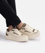 Championes urbanos Renner de diseño robusto con suela voluminosa, confeccionados en poliuretano color beige con recortes contrastantes en marrón y detalles en negro. Cuentan con cierre de cordones, estabilizador trasero y mezcla de materiales con inserciones de malla.