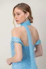 Vestido largo de fiesta en tul bordado con lentejuelas celestes, silueta ceñida, escote con tirantes caídos y tajo frontal.