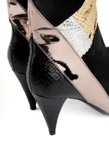 Bota corta de caña media color negro con paneles de cuero sintético texturizado y detalles metalizados en dorado y plateado. Tiene taco fino y punta en pico.