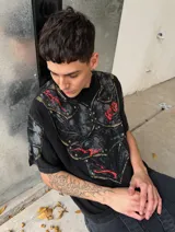 Remera de algodón con efecto acid wash y corte boxy fit. Presenta un estampado frontal que simula una armadura medieval con detalles en rojo y remaches, extendiéndose hacia las mangas.