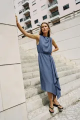 Vestido midi de color azul, confeccionado con lino. Presenta cuello redondo, manga sisa y diseño sin mangas. Cuenta con bajo asimétrico y detalle de vuelo en la parte frontal.