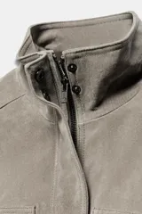 Cazadora cropped de piel con cuello subido, manga larga y trabillas en los hombros. Presenta bolsillos delanteros de plastrón y cierre frontal con cremallera y botones a presión ocultos.