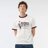 Camiseta blanca de manga corta con ribetes en contraste de color bordó en el cuello y los puños. Presenta un estampado gráfico frontal con la inscripción "Stephen's Running Club Est. 88 Sacramento" y la silueta de un corredor.