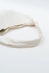 Cartera tipo hobo bag color negro, con detalles de tachas plateadas en los bordes y un charm colgante en forma de corazón también con tachas.