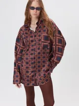 Camisa de seda con cuello camisero, manga larga y bolsillo frontal. Presenta un diseño estampado geométrico de cuadrados en tonos marrones y azul oscuro.