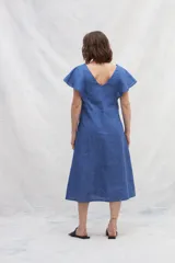 Vestido midi de lino en color azul, con escote en V tanto en el frente como en la espalda. Presenta mangas cortas con vuelo, silueta amplia y cintas verticales a contratono en el frente que estilizan la figura. Incluye bolsillos laterales.