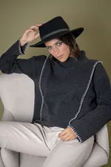 Buzo de cuello alto confeccionado en lana, color gris oscuro, con detalles de costuras bordadas en hilo blanco en los laterales y puños. Presenta un diseño holgado y mangas largas.
